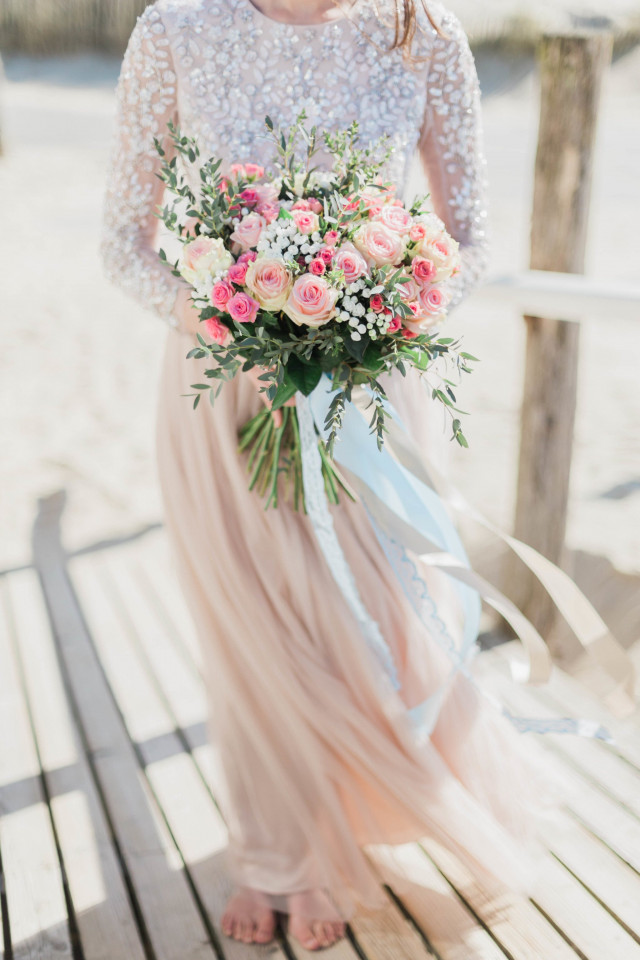 Bruid op het strand met een groot bruidsboeket met verschillende soorten roze rozen