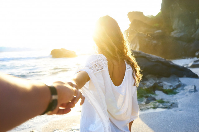 Checkliste Flitterwochen - Braut nimmt ihren Bräutigam an die Hand und blickt Richtung Sonnenuntergang am Meer
