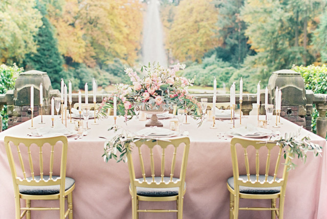 Gedekte tafel met roze laken, grote bloemen en gouden stoelen