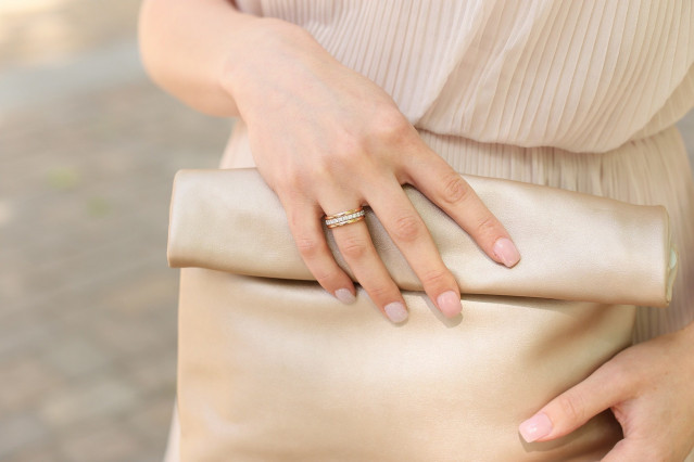 Handen die een gouden tasje vasthouden met nude bruidsnagels met glitters